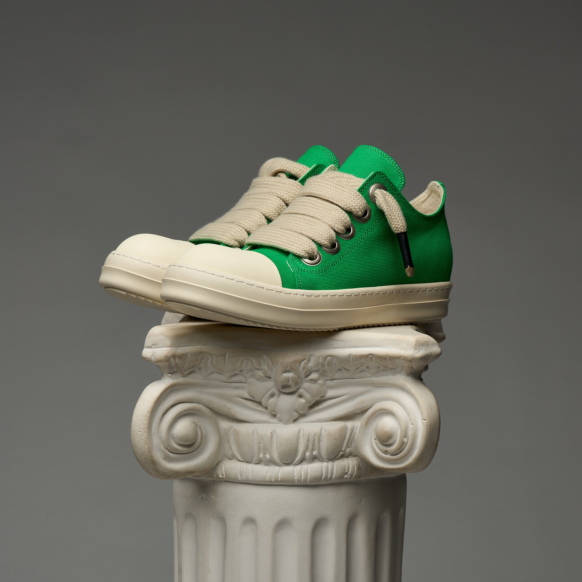 DUAA Green and beige sneakers on an ornate stone pedestal against a gray background
