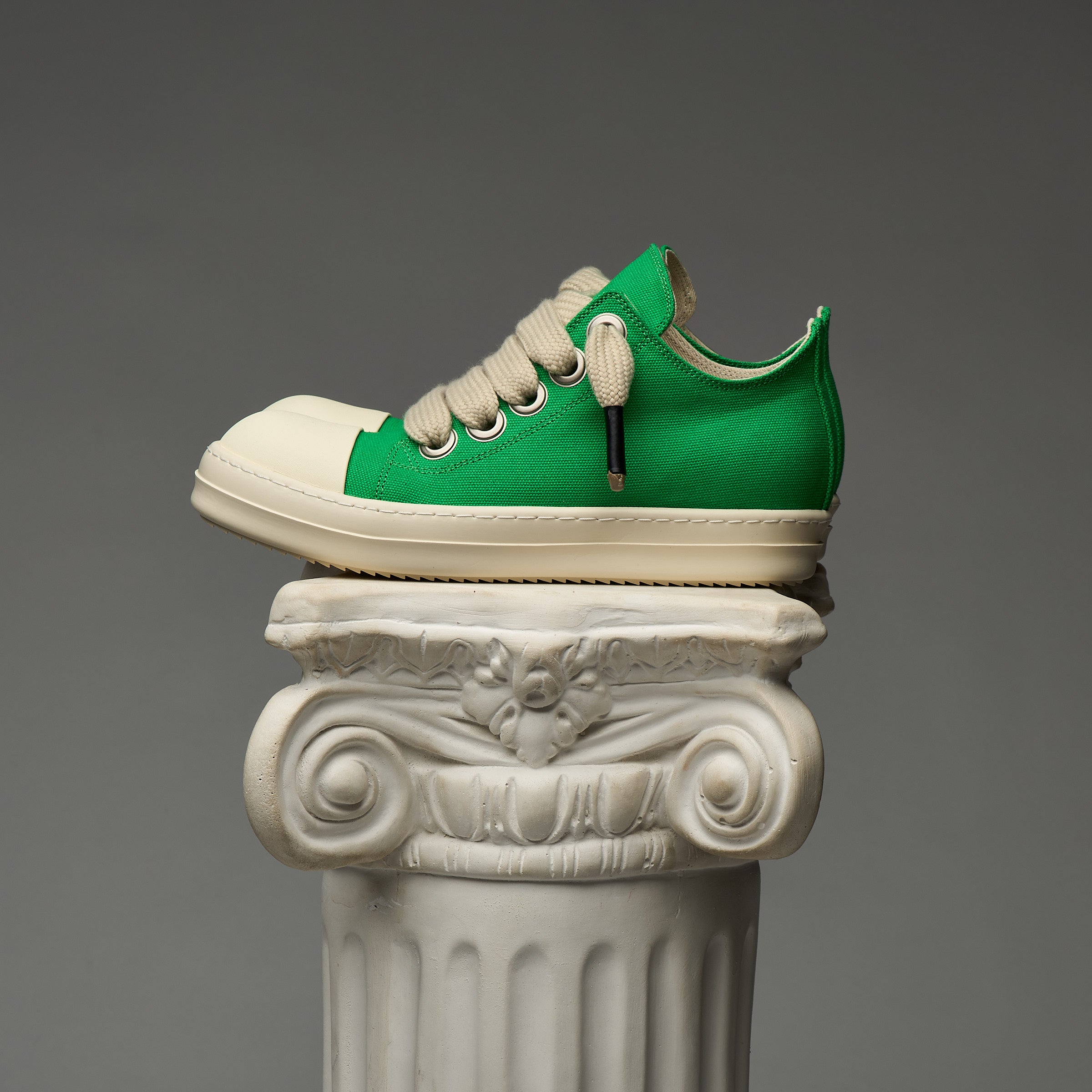 DUAA Green and white sneaker on a decorative column against a gray background