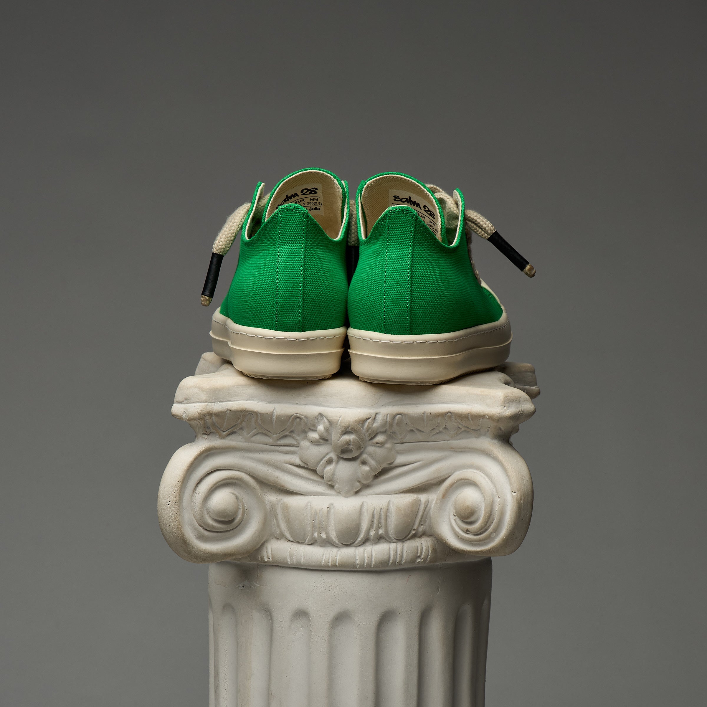 DUAA Green sneakers with white soles on a decorative column against a gray background