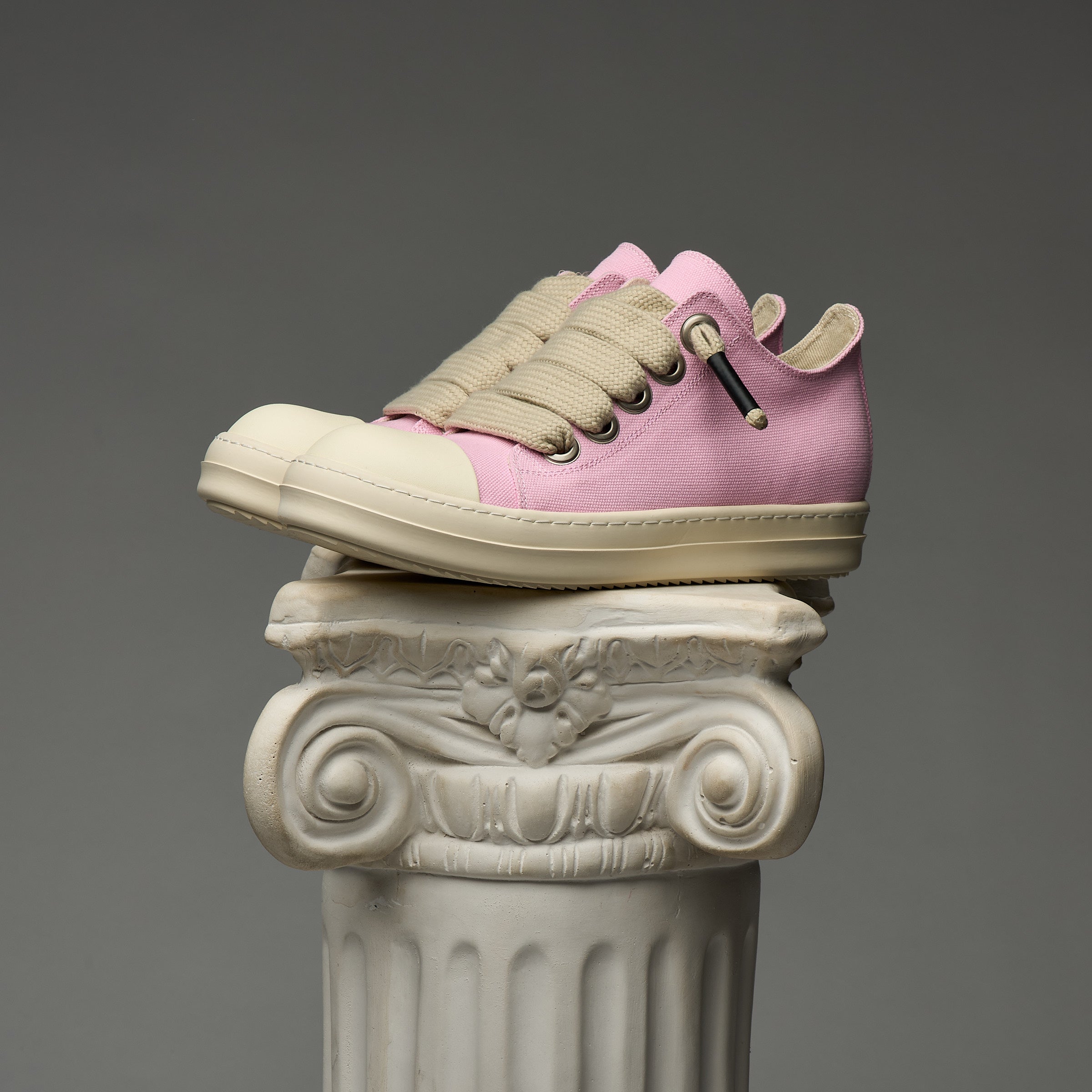 Pink DUAA sneakers with beige accents on a decorative column against a gray background
