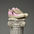 Pink DUAA sneakers with beige laces on a decorative column against a gray background