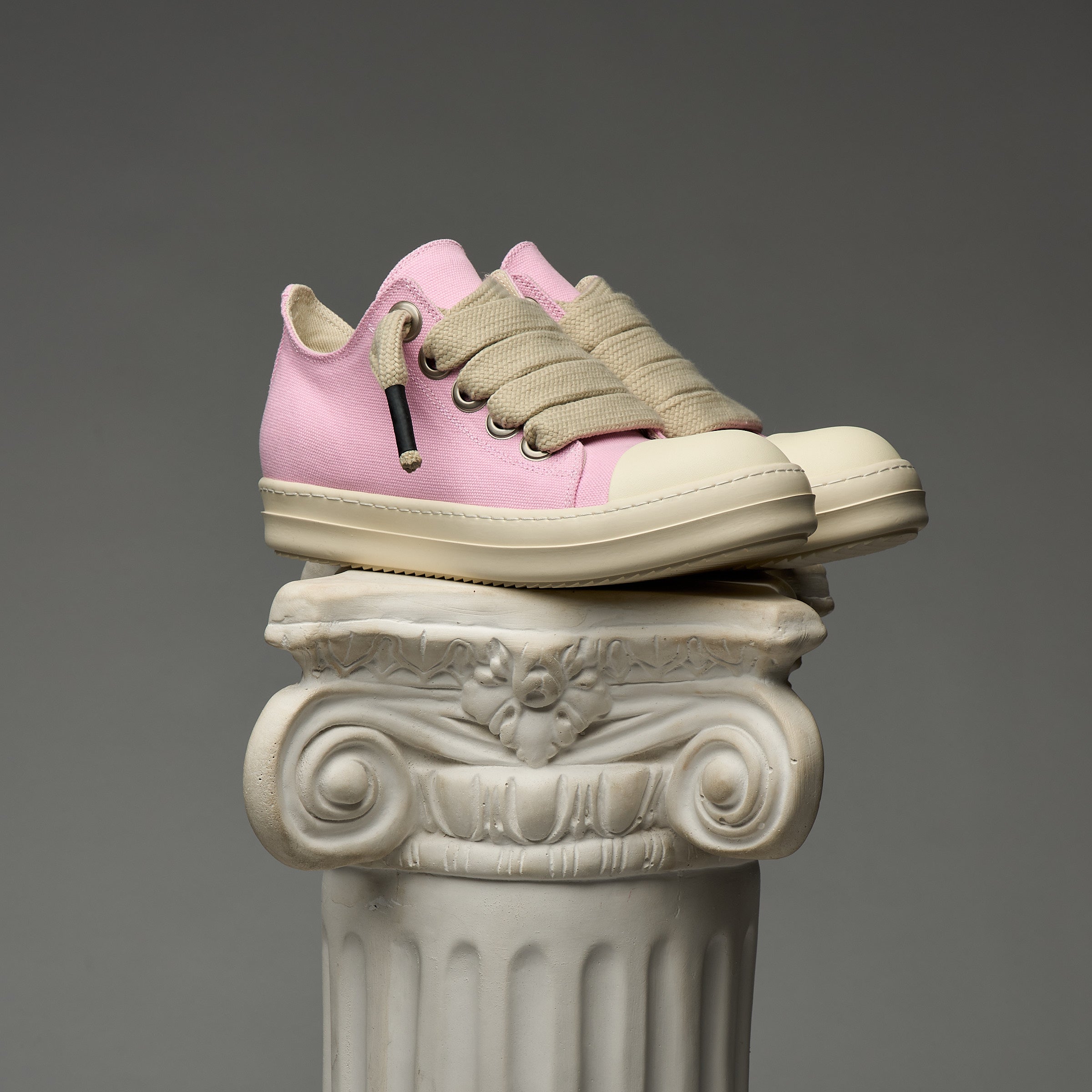 Pink DUAA sneakers with beige laces on a decorative column against a gray background