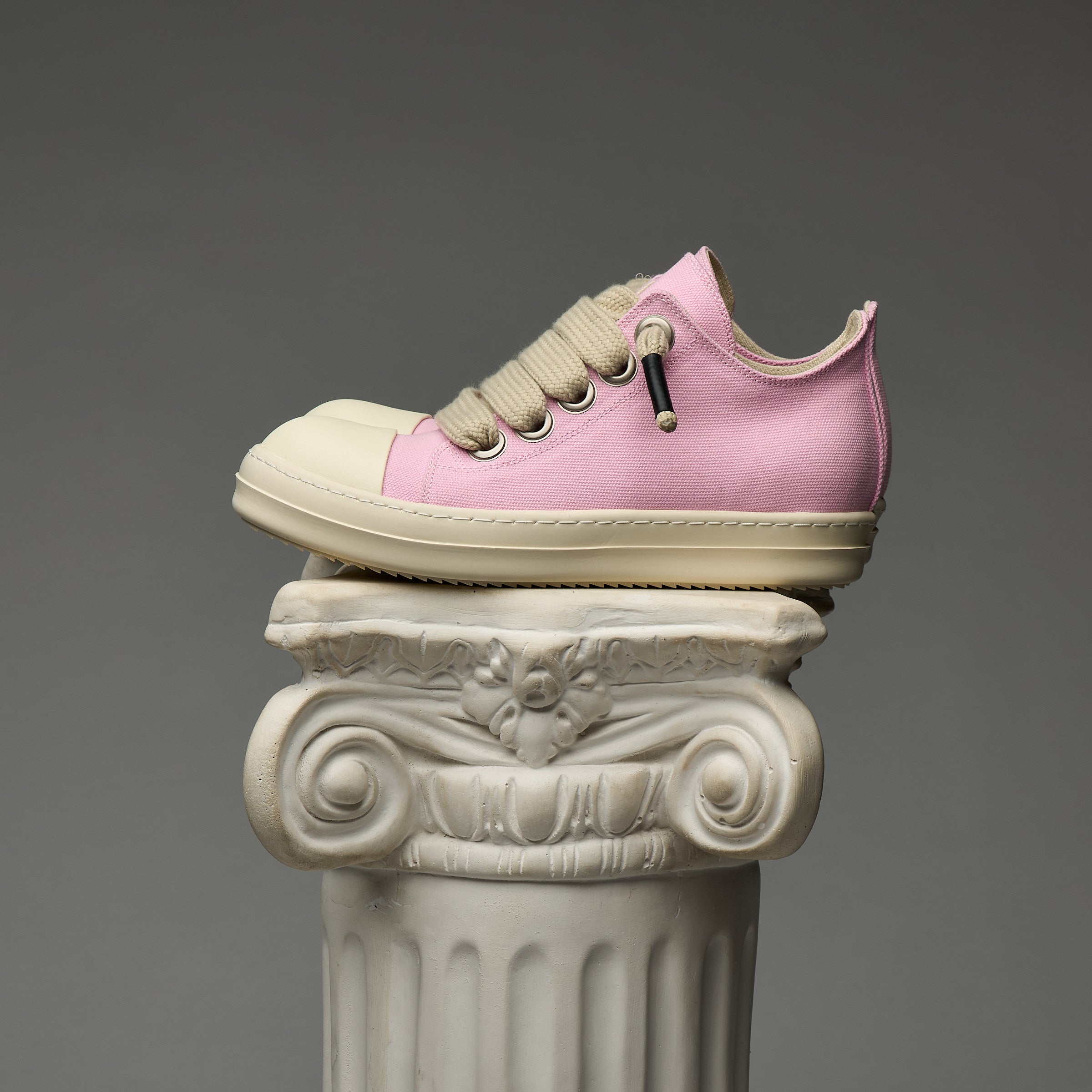 DUAA Pink and beige sneaker on a decorative column against a gray background