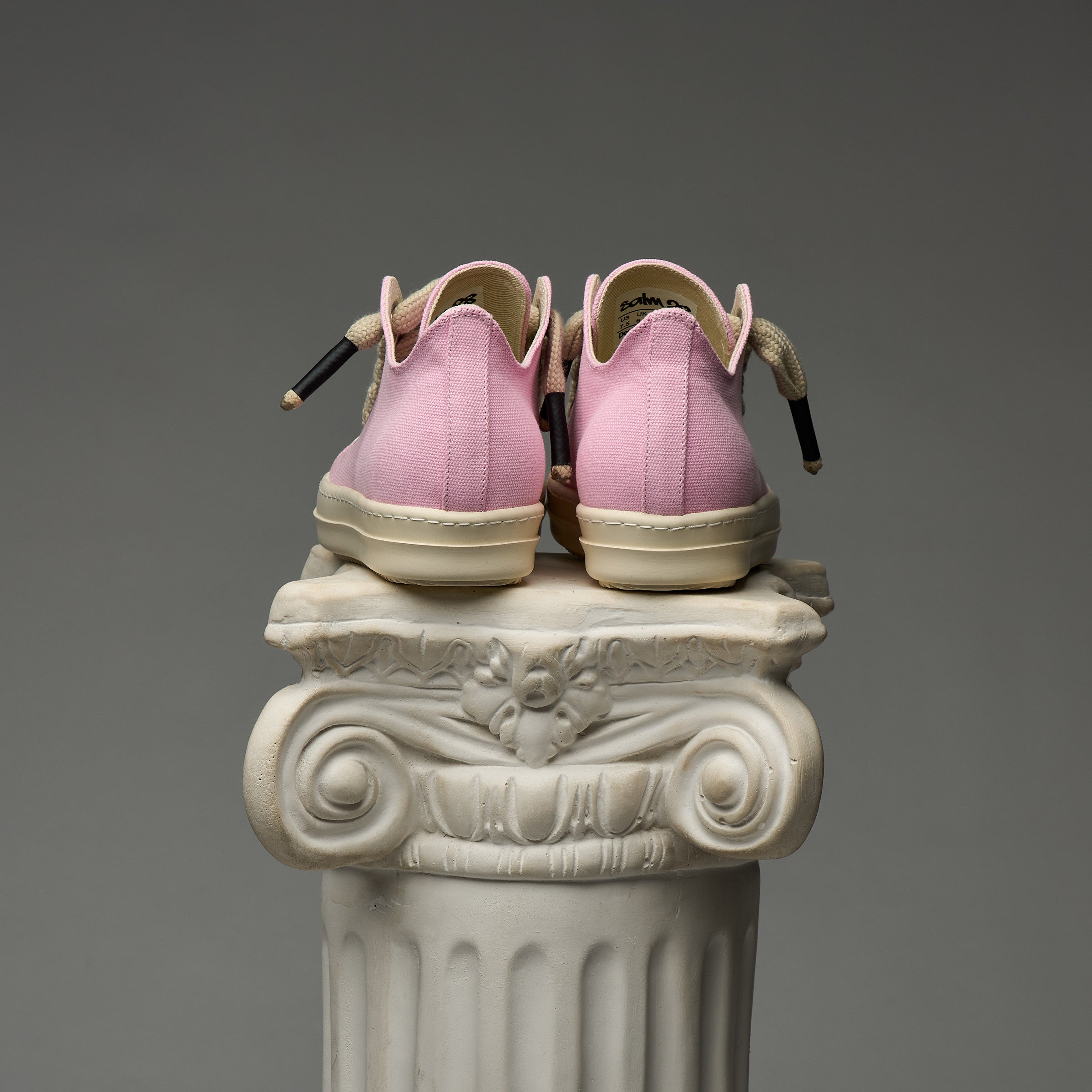 DUAA Pink sneakers on a decorative white column against a gray background