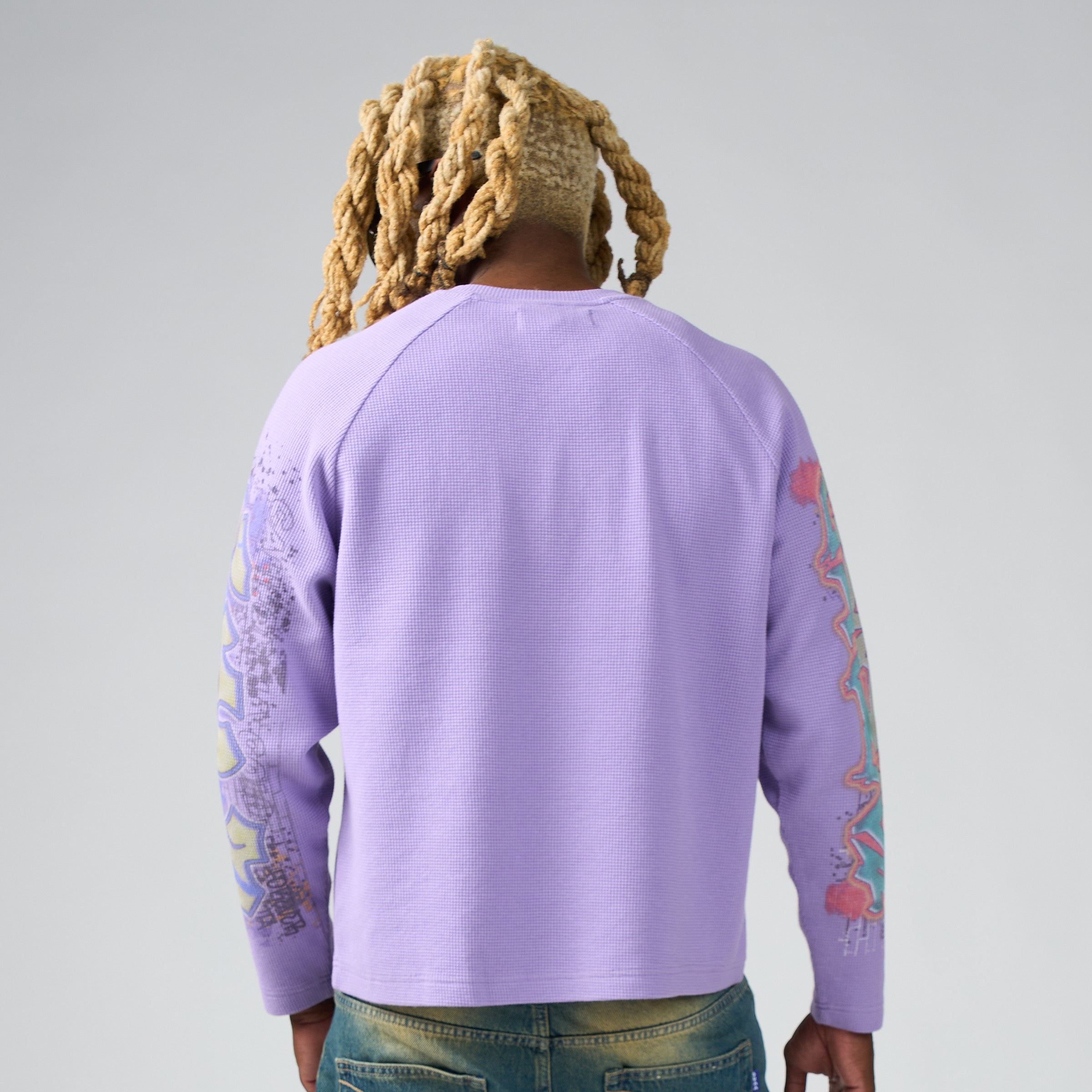 Person wearing a purple DUAA sweatshirt with colorful designs on sleeves against a plain background