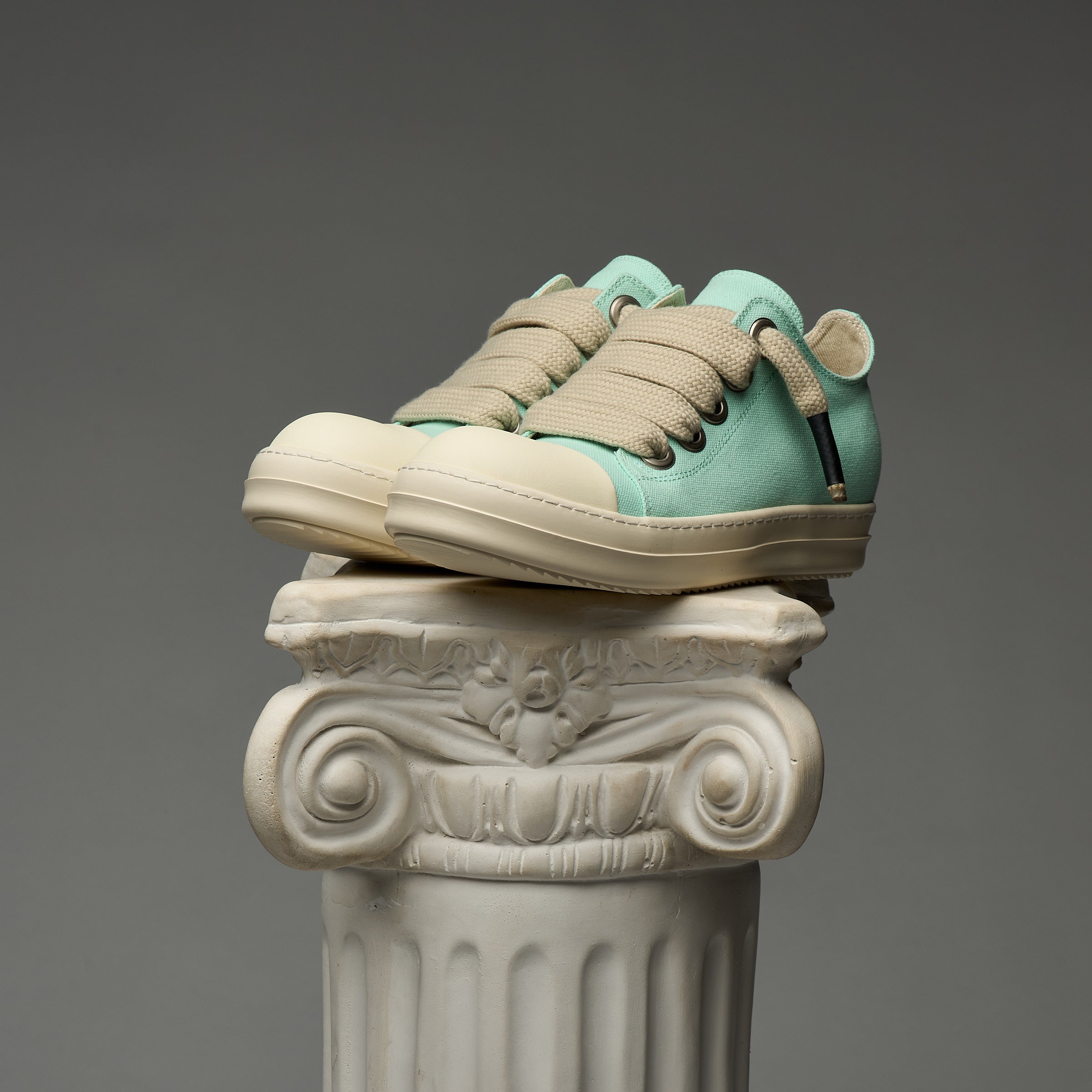 Mint and beige DUAA sneakers on a decorative column against a gray background