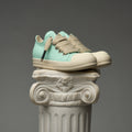 Pair of mint and beige DUAA sneakers stacked on a classical column against a gray background