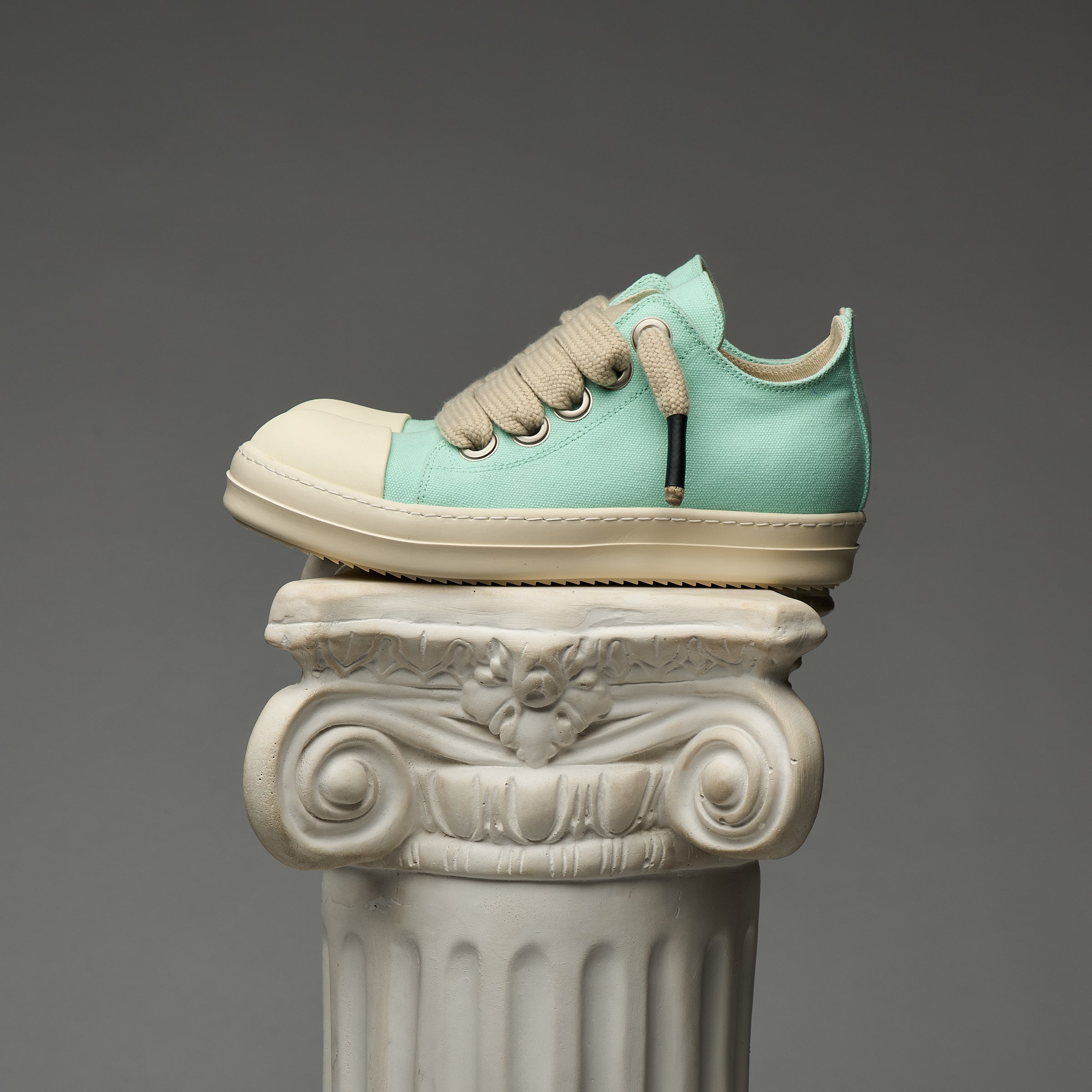 Mint and beige DUAA sneaker on a decorative column against a gray background