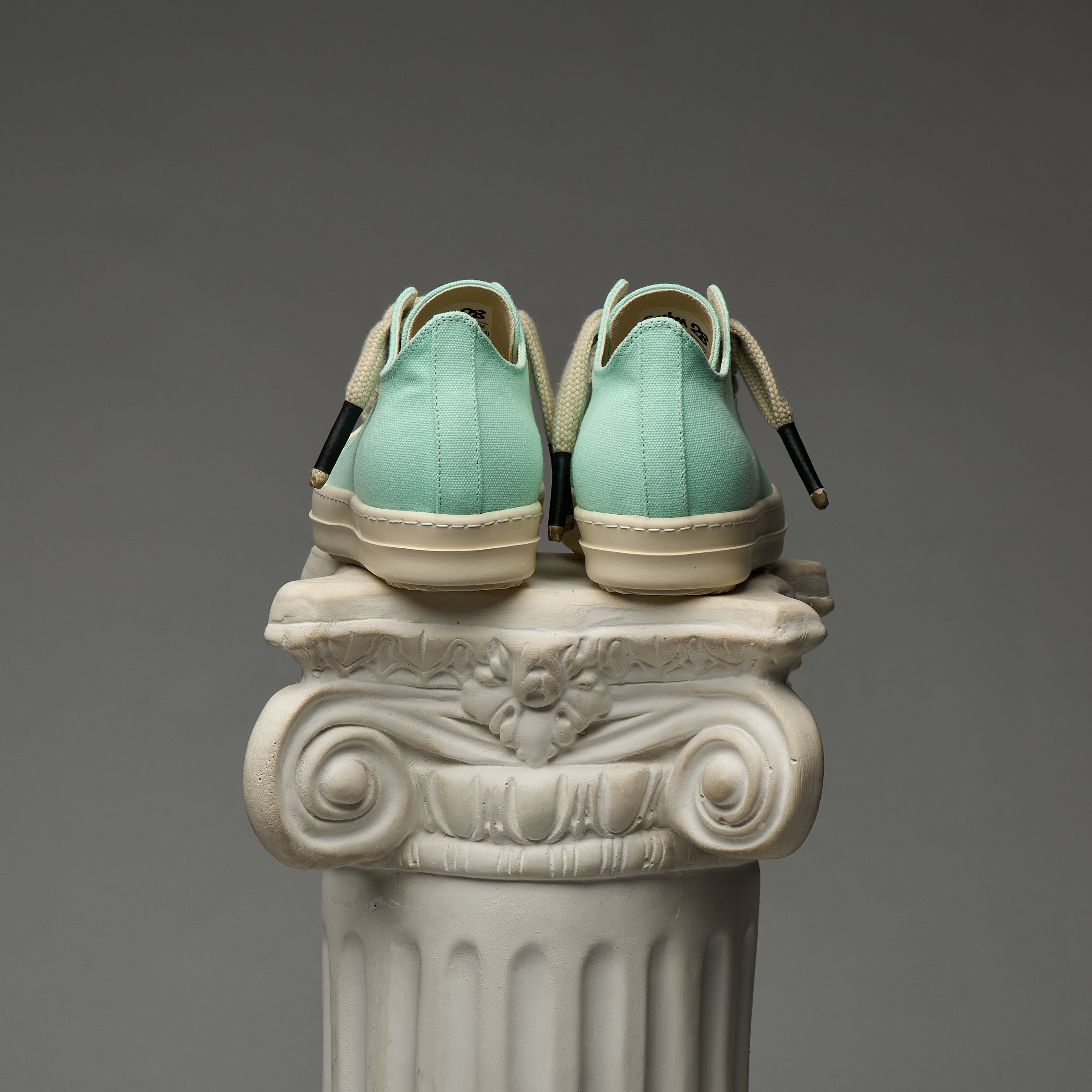 Pair of mint DUAA sneakers on a decorative column against a gray background