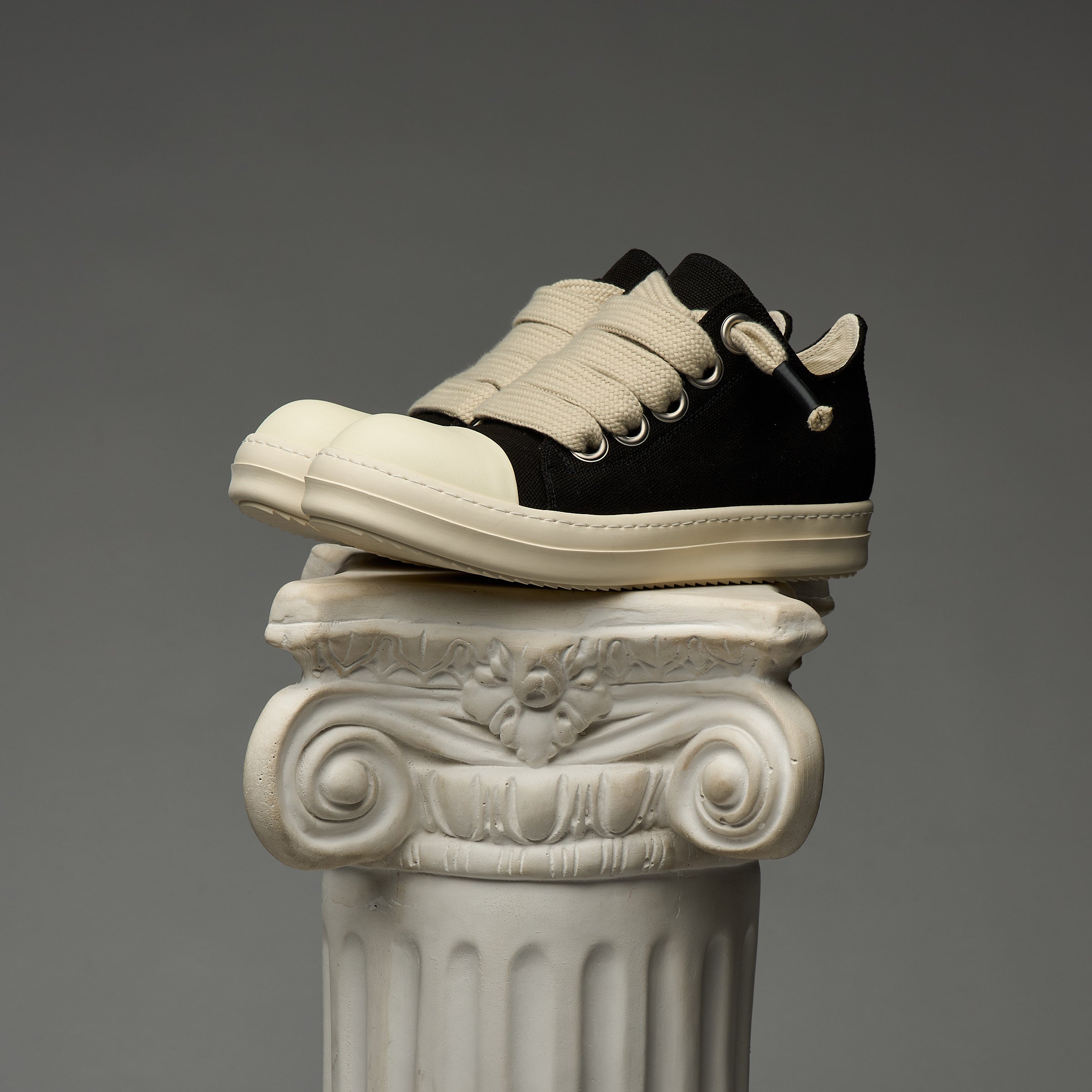DUAA Black and white sneakers on an ornate stone column against a gray background