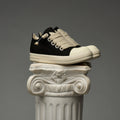 DUAA Black and white sneakers on an ornate column against a gray background