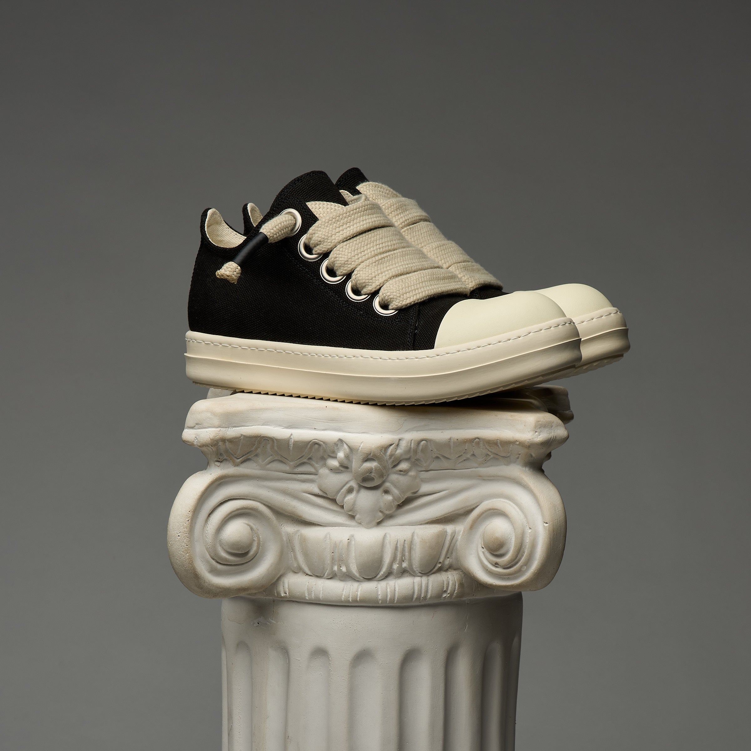 DUAA Black and white sneakers on an ornate column against a gray background