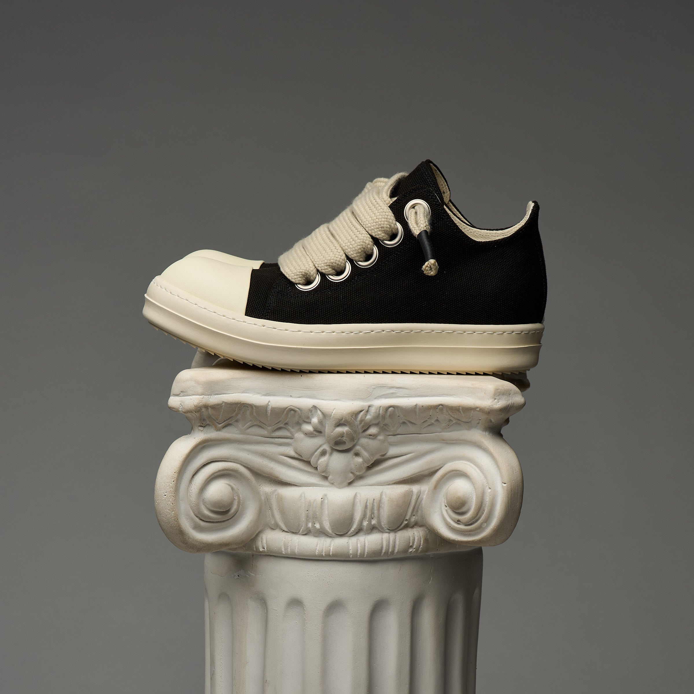 DUAA Black and white sneaker on a decorative column against a gray background