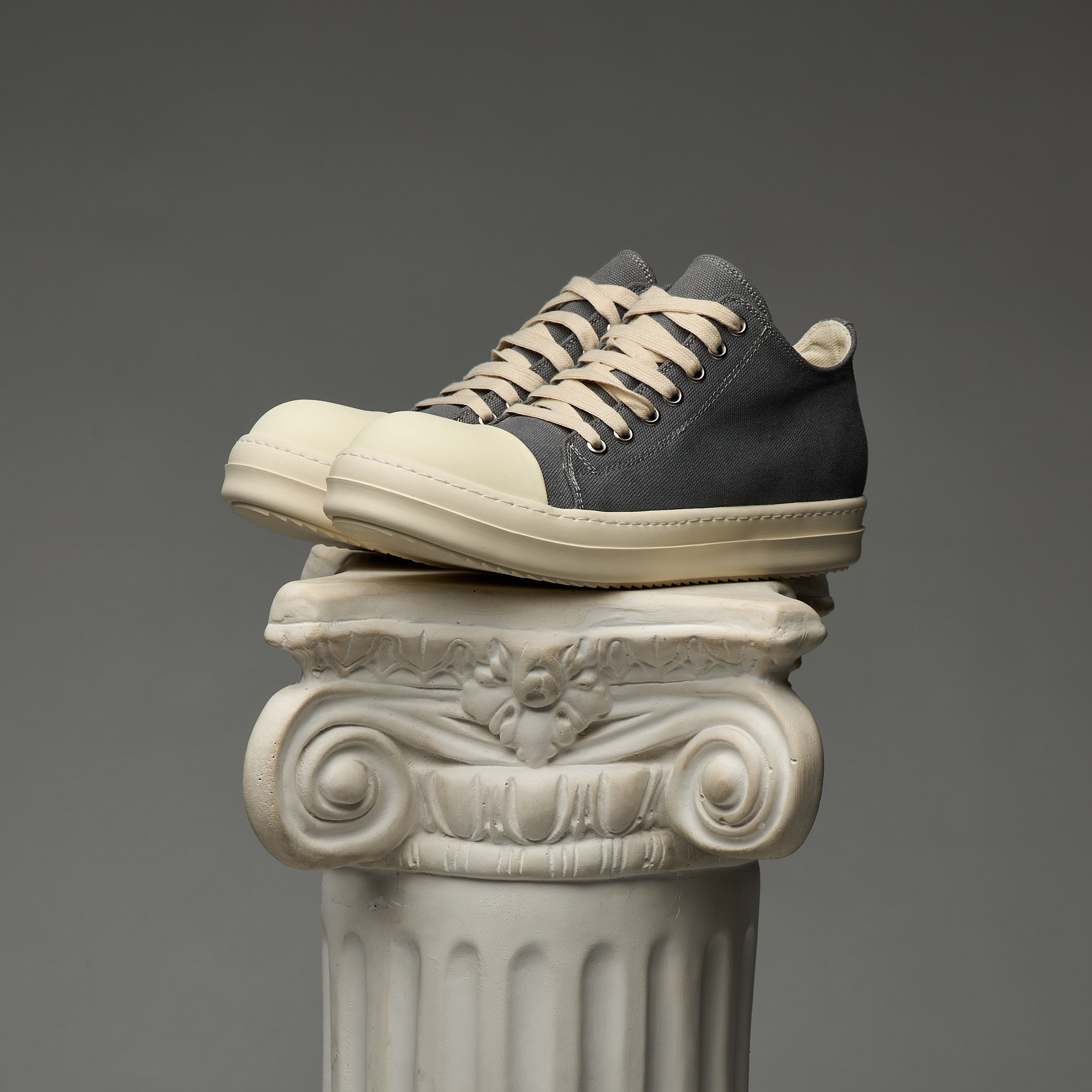 Pair of DUAA gray and beige sneakers on a decorative column against a gray background
