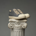 Pair of DUAA sneakers stacked on a decorative column against a gray background
