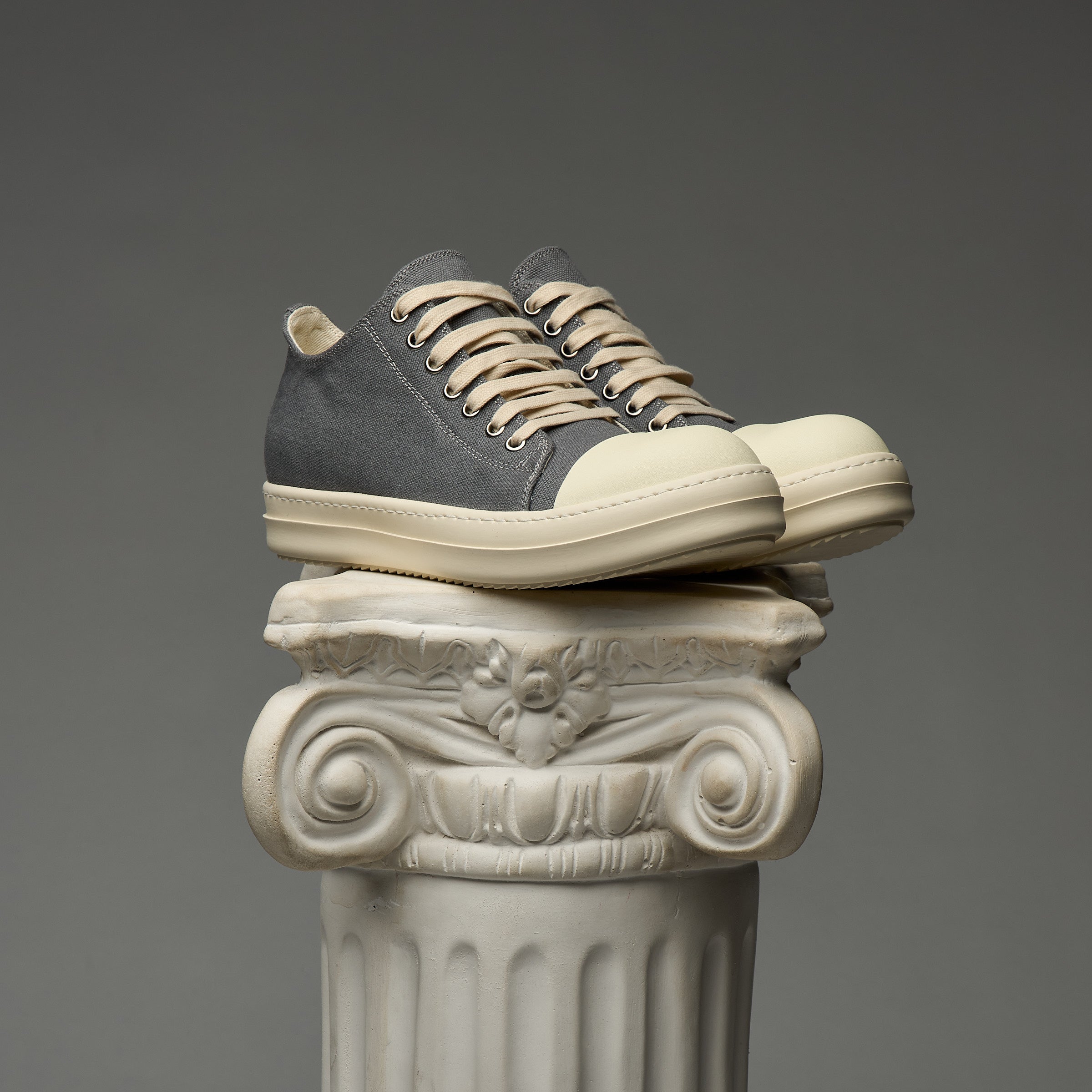 Pair of DUAA sneakers stacked on a decorative column against a gray background