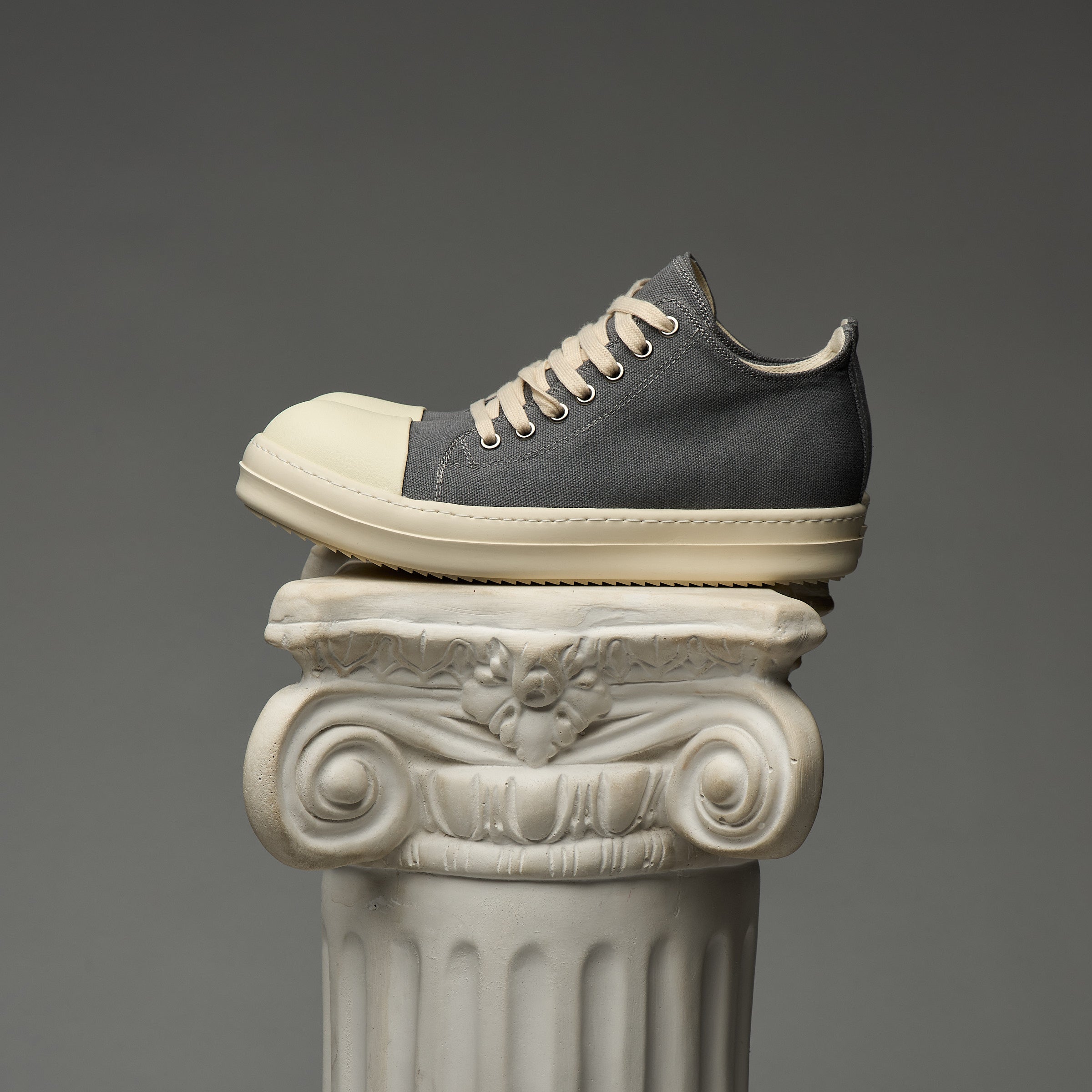 Gray and white DUAA sneaker on a decorative column against a gray background