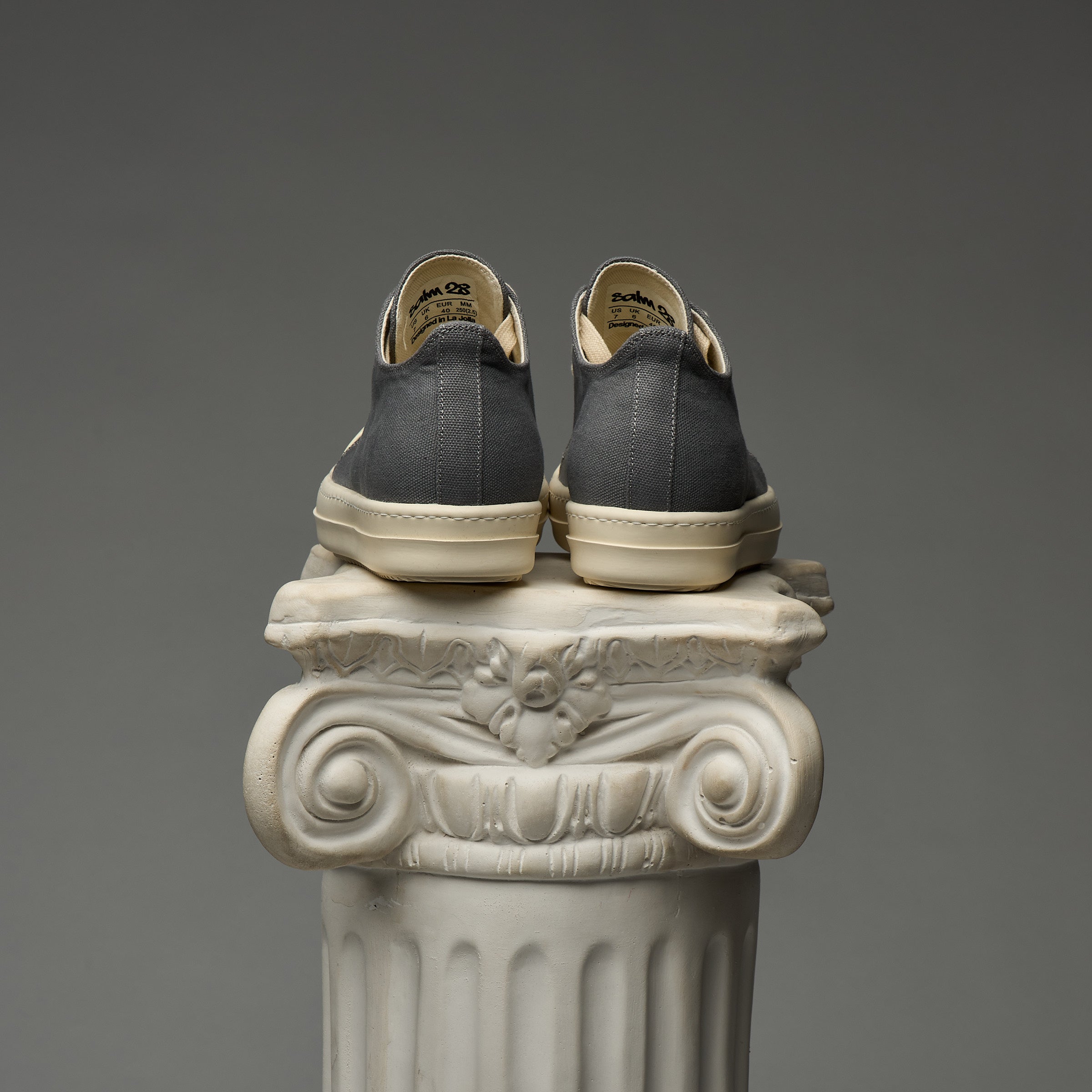 Gray DUAA sneakers with beige soles on an ornate white column against a gray background