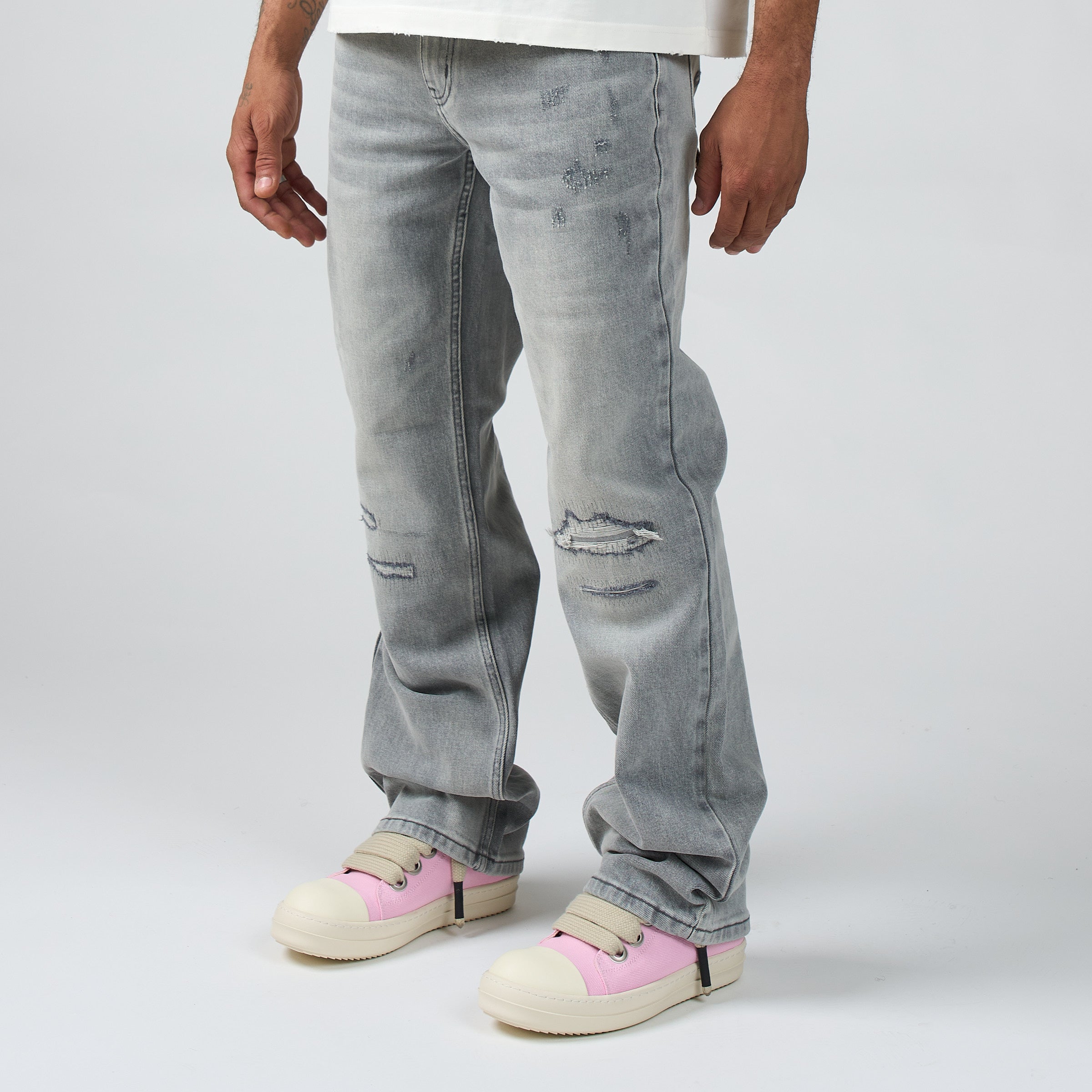 A person wearing DUAA light gray distressed jeans with ripped details on the thighs and knees, paired with DUAA pink and cream platform sneakers, shown from the waist down against a light gray studio background.