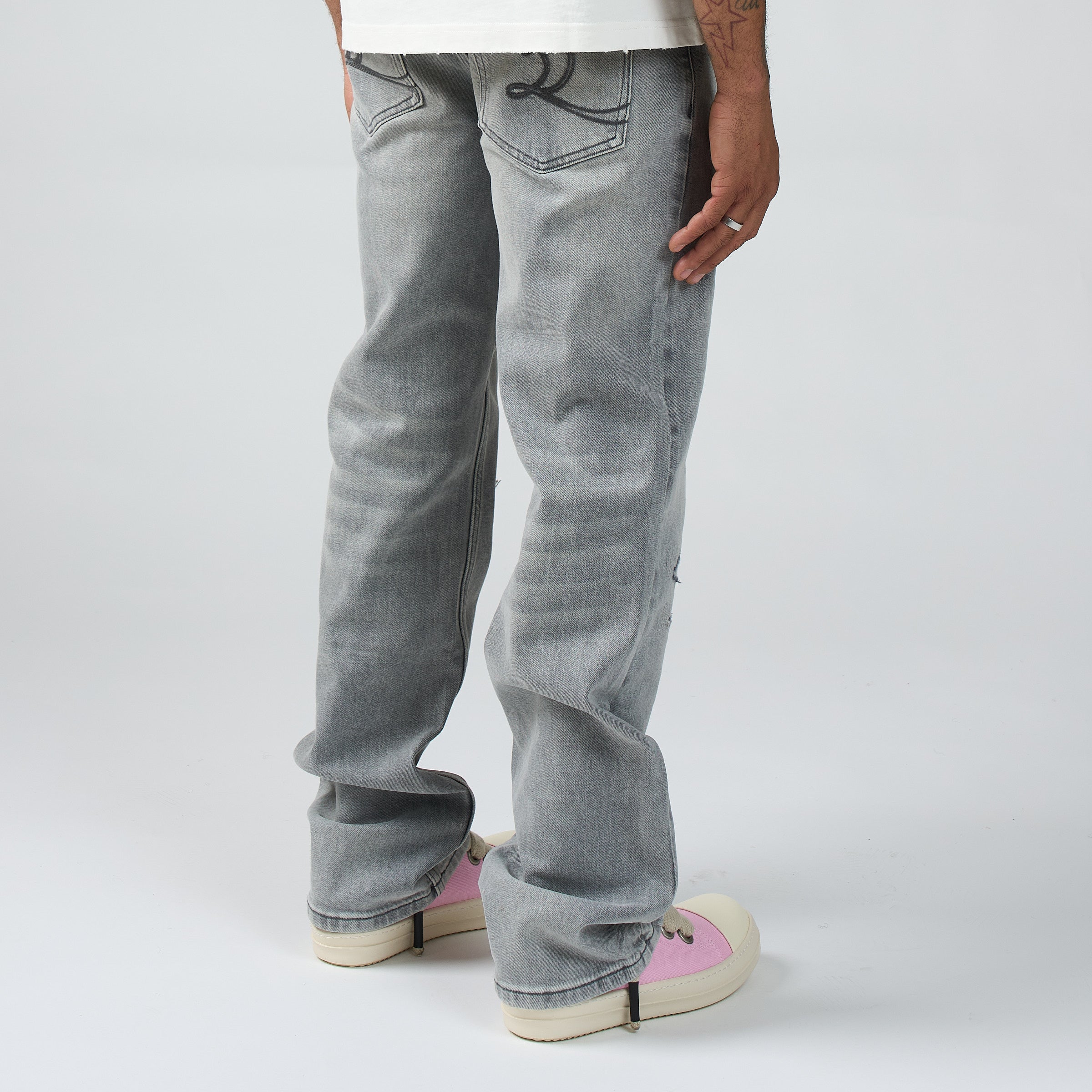 A person shown from the waist down wearing DUAA light gray washed denim jeans and DUAA pink-and-white sneakers against a plain light gray studio background.