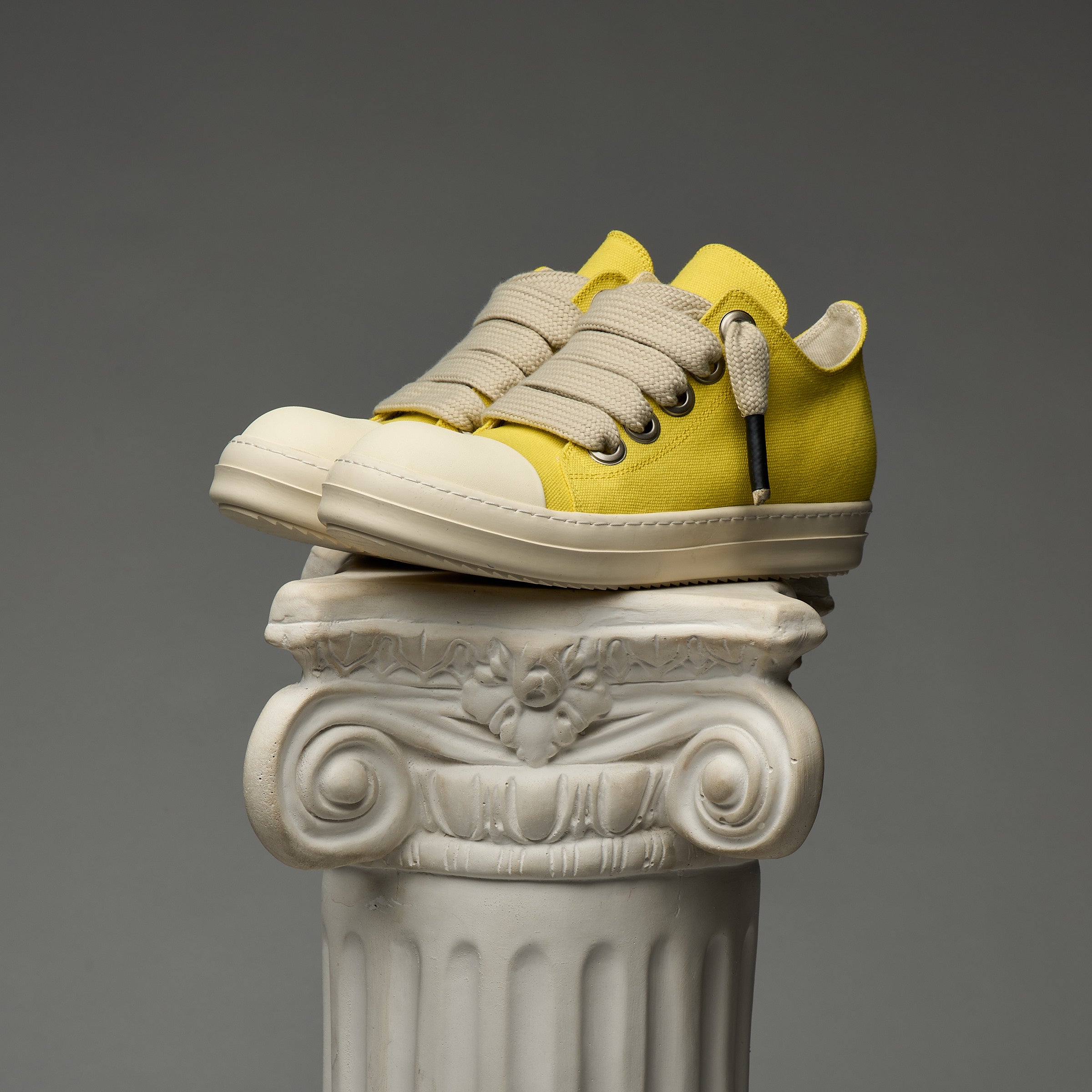 DUAA Yellow and beige sneakers on an ornate white column against a gray background