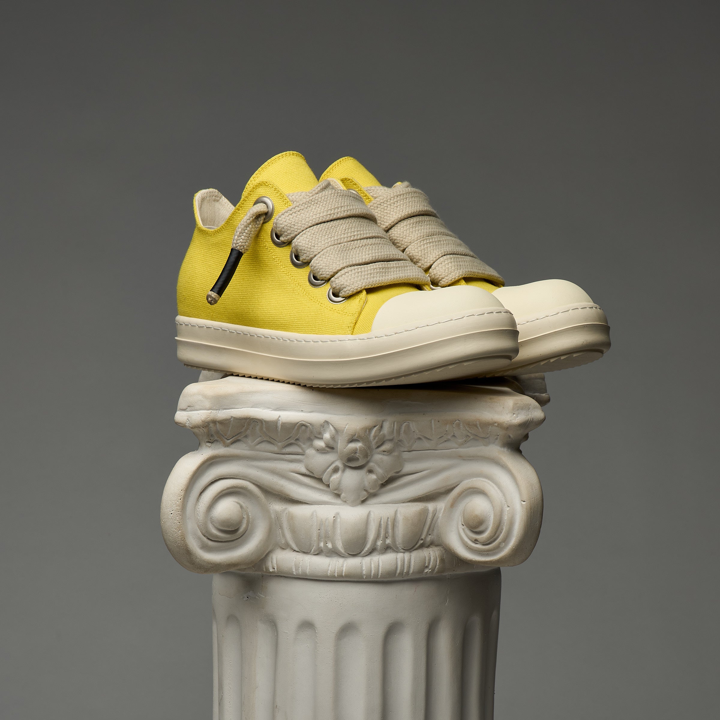 DUAA Yellow sneakers on a decorative column against a gray background