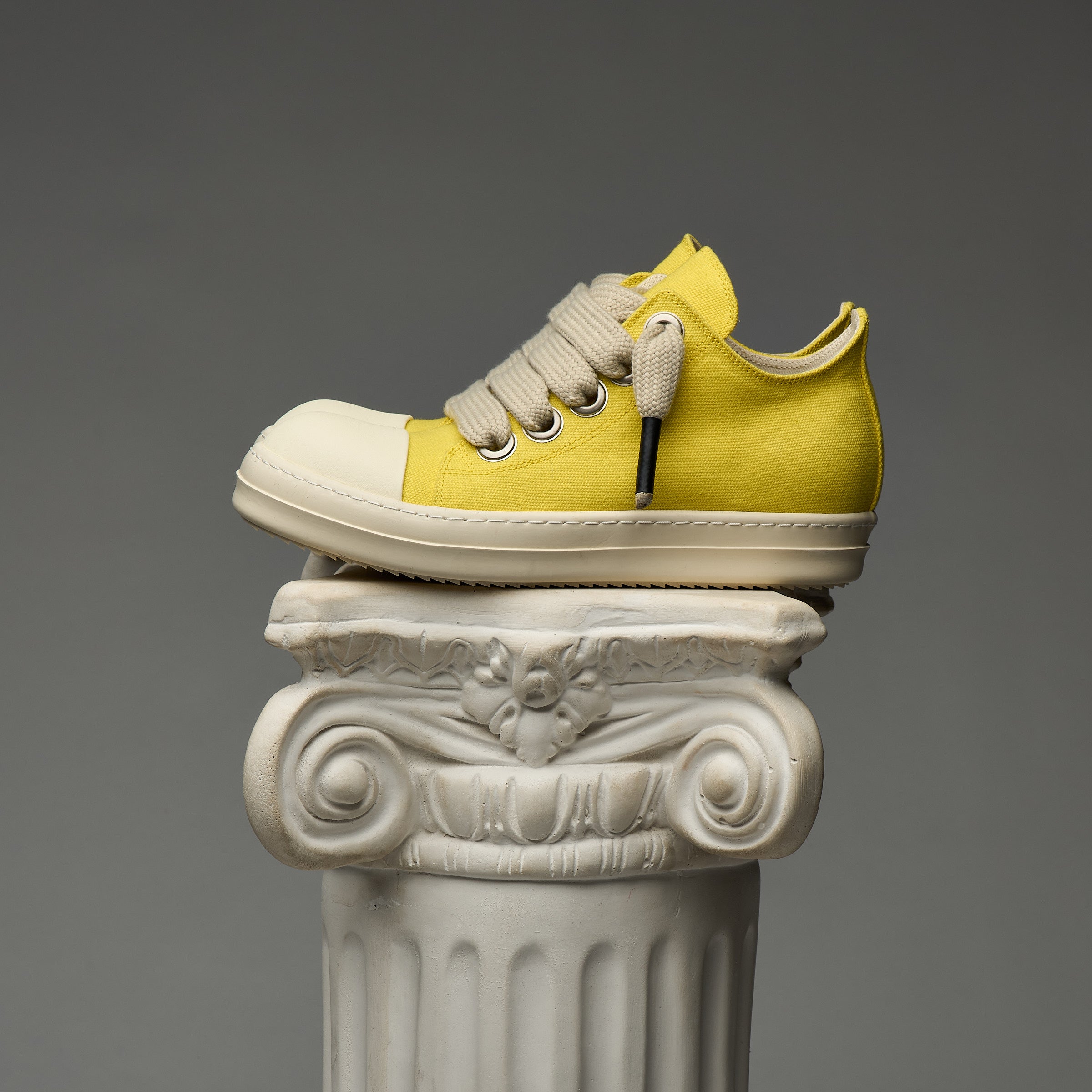 DUAA Yellow sneaker on a decorative column against a gray background