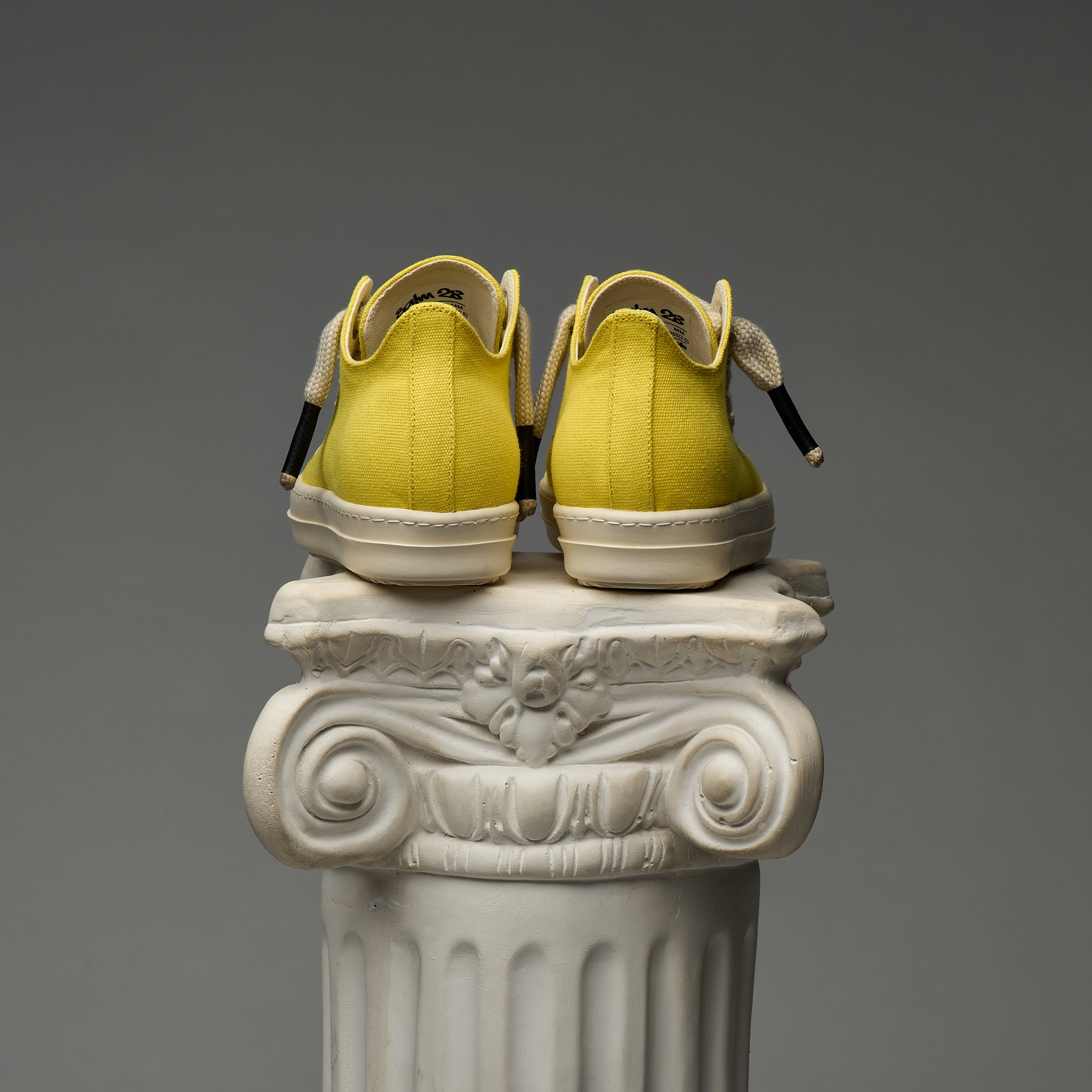 DUAA Yellow sneakers on a decorative white column against a gray background