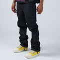 Person wearing DUAA black wax coated jeans and yellow sneakers on a light gray background