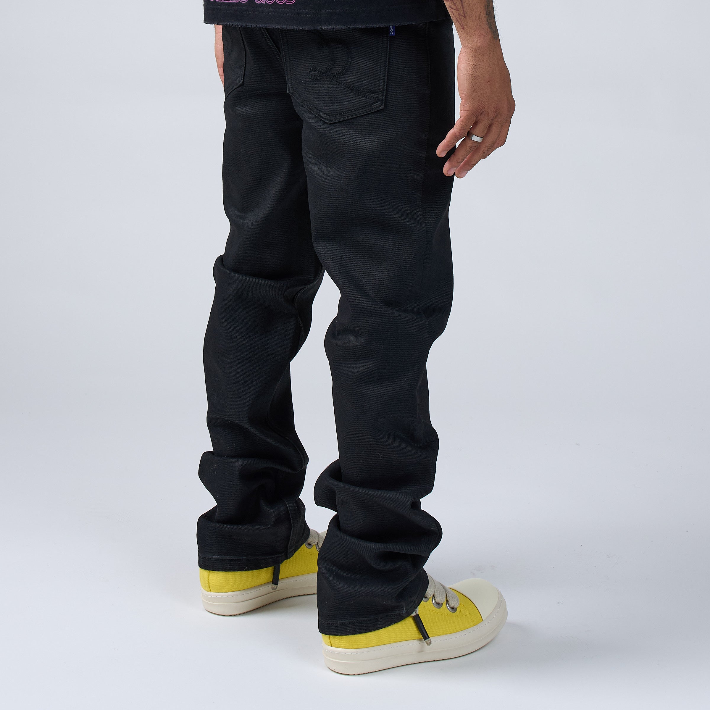 Person wearing DUAA black wax pants and yellow sneakers on a white background