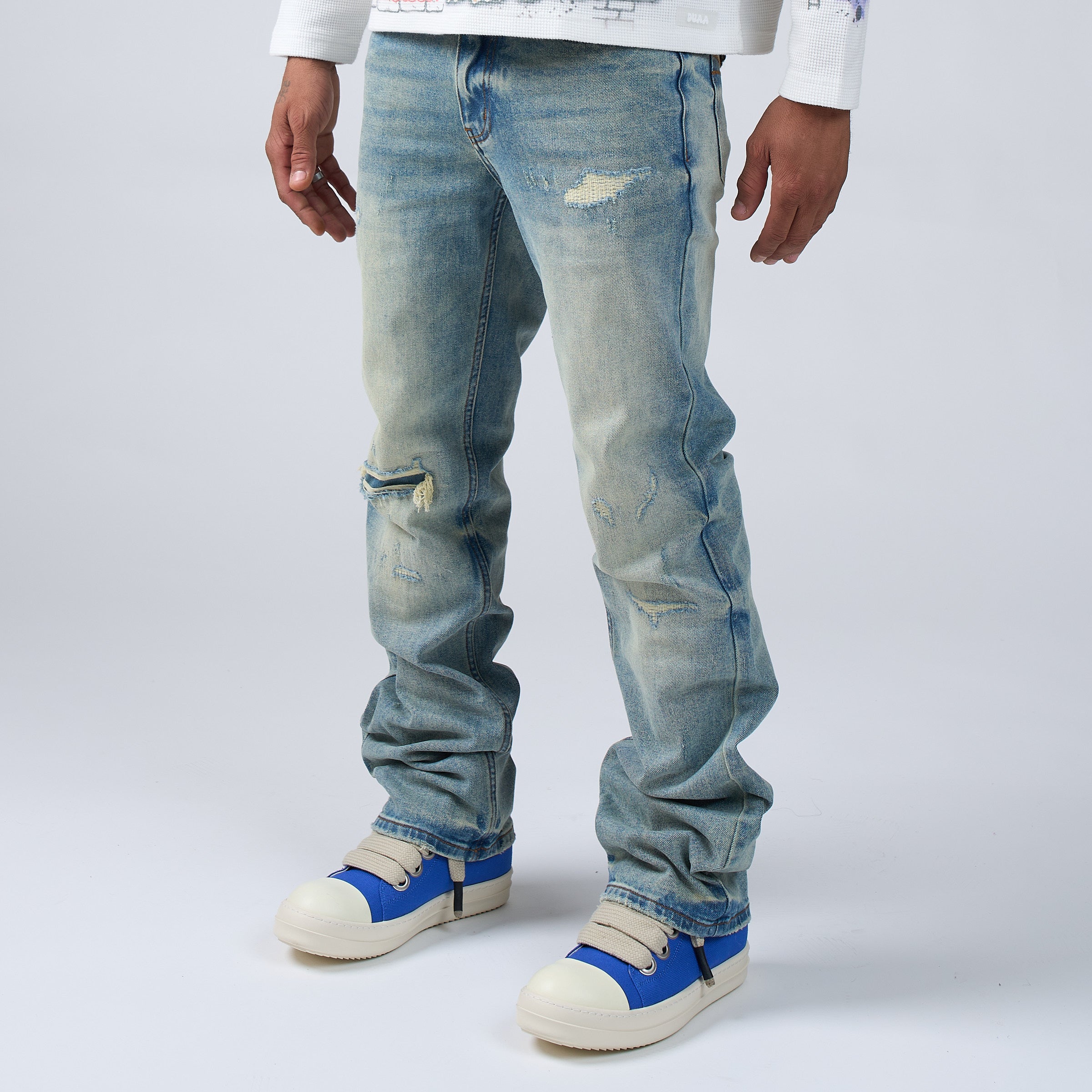 Person wearing DUAA distressed blue jeans and blue sneakers on a white background