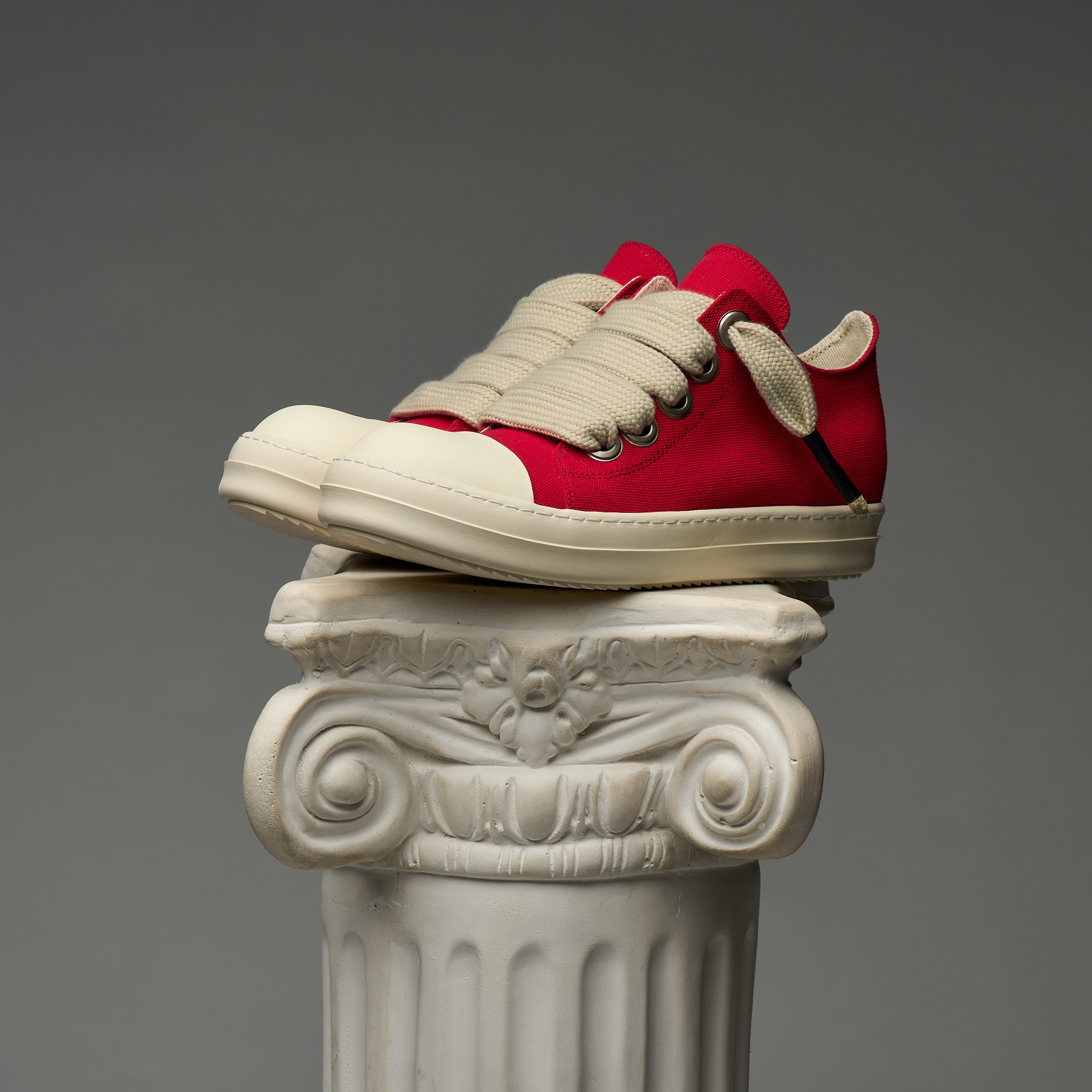 DUAA Red and white sneakers on a decorative column against a gray background