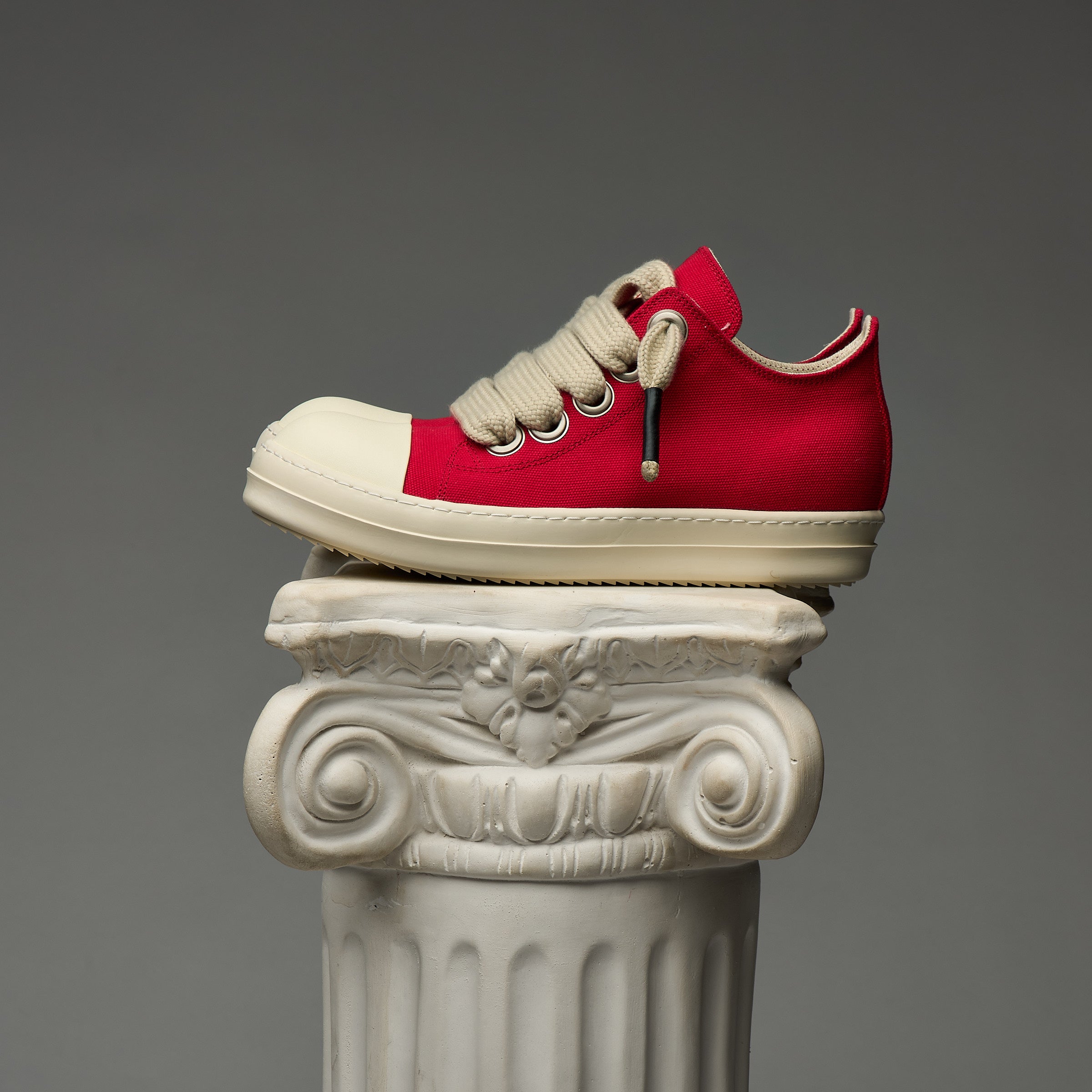 DUAA Red and white sneaker on a decorative column against a gray background