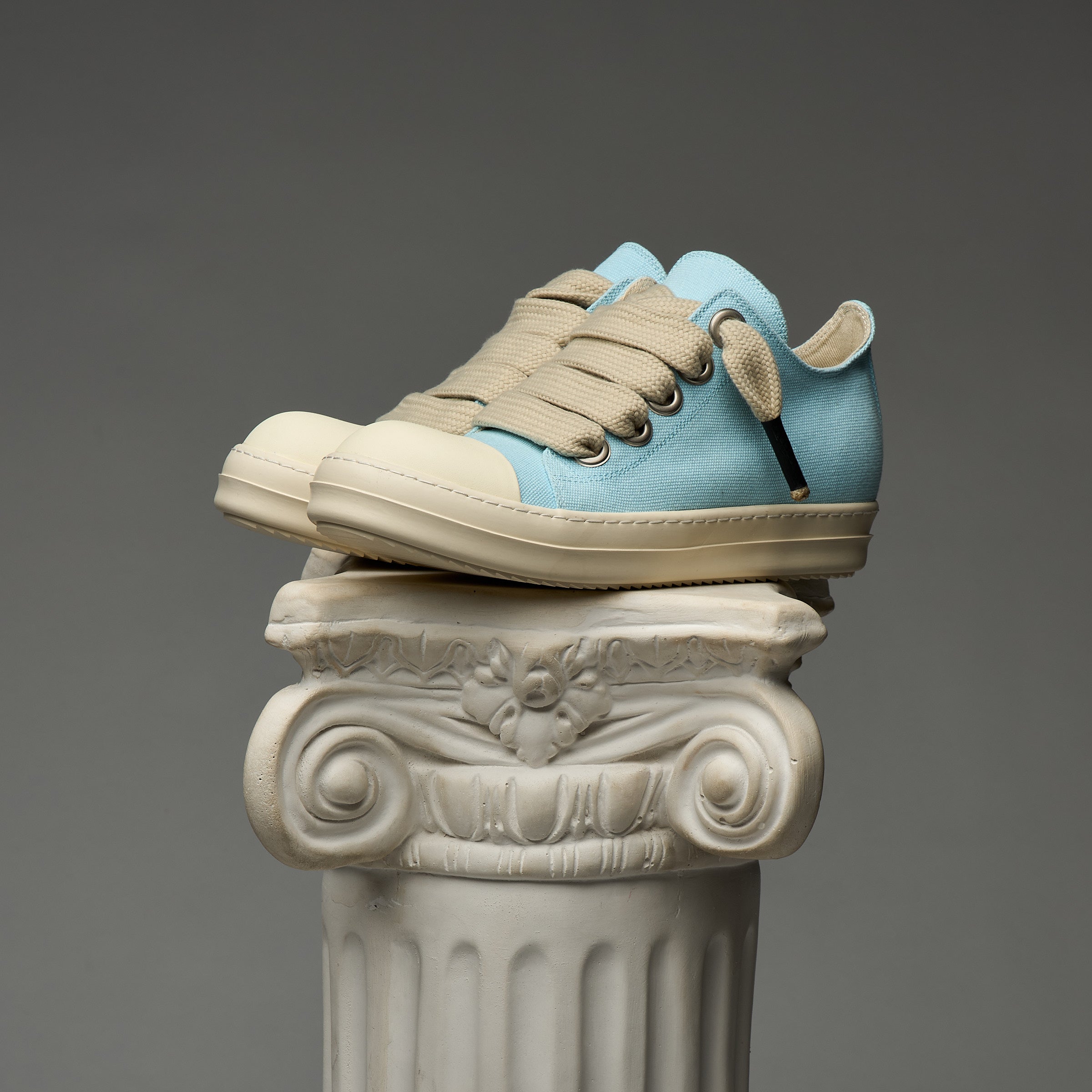 Blue and beige DUAA sneakers on an ornate column against a gray background