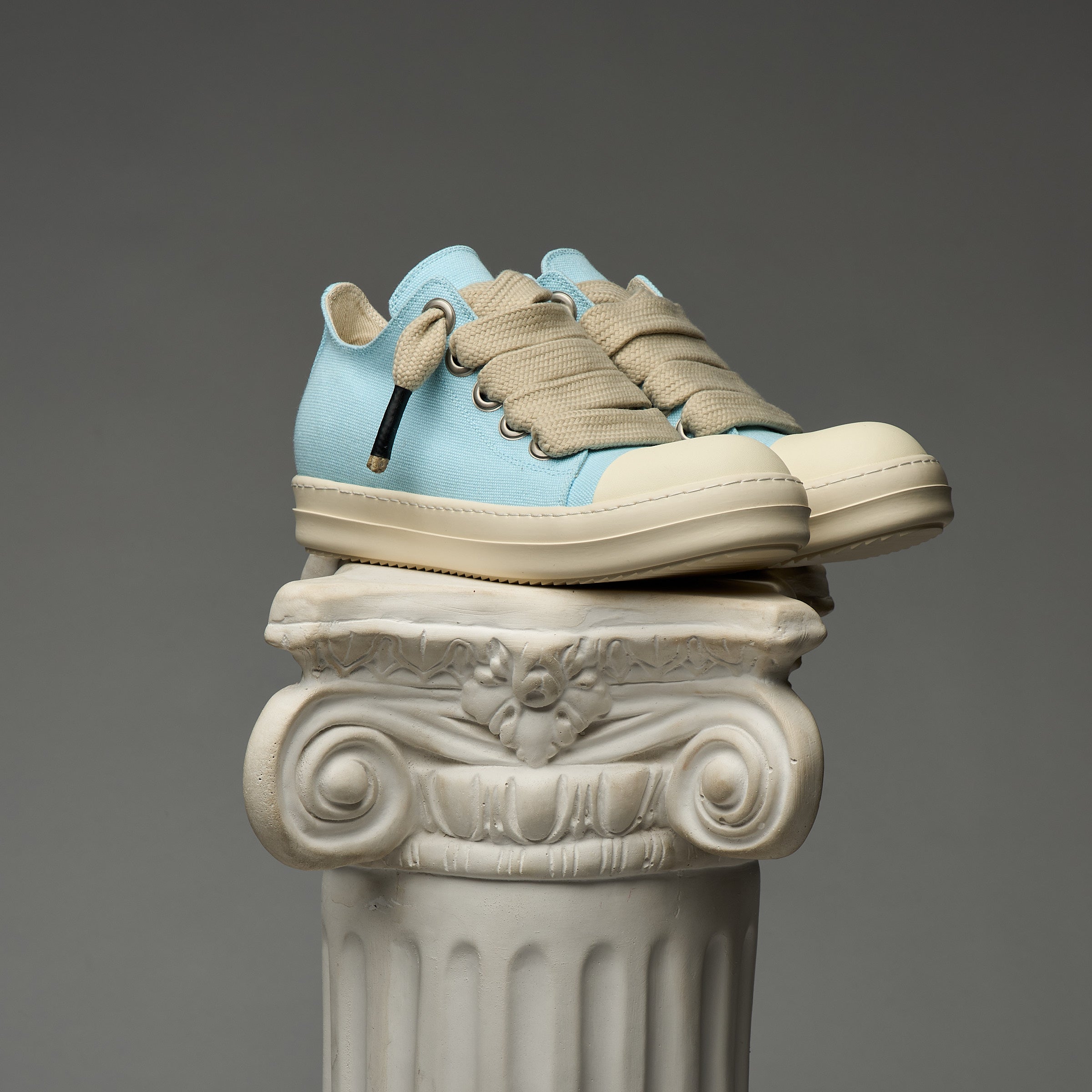 Blue and beige DUAA sneakers on a decorative column against a gray background