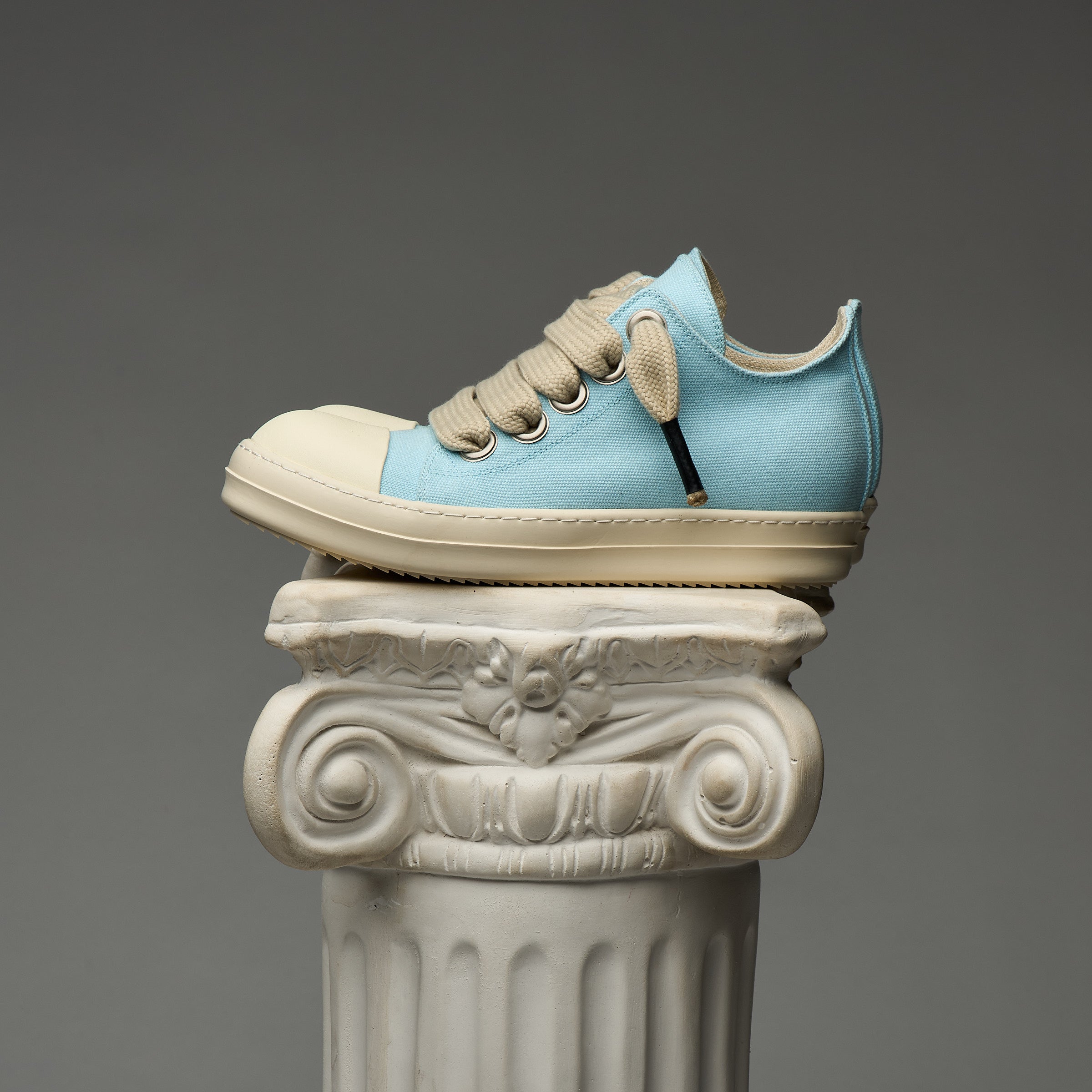 Blue and beige DUAA sneaker on an ornate stone column against a gray background