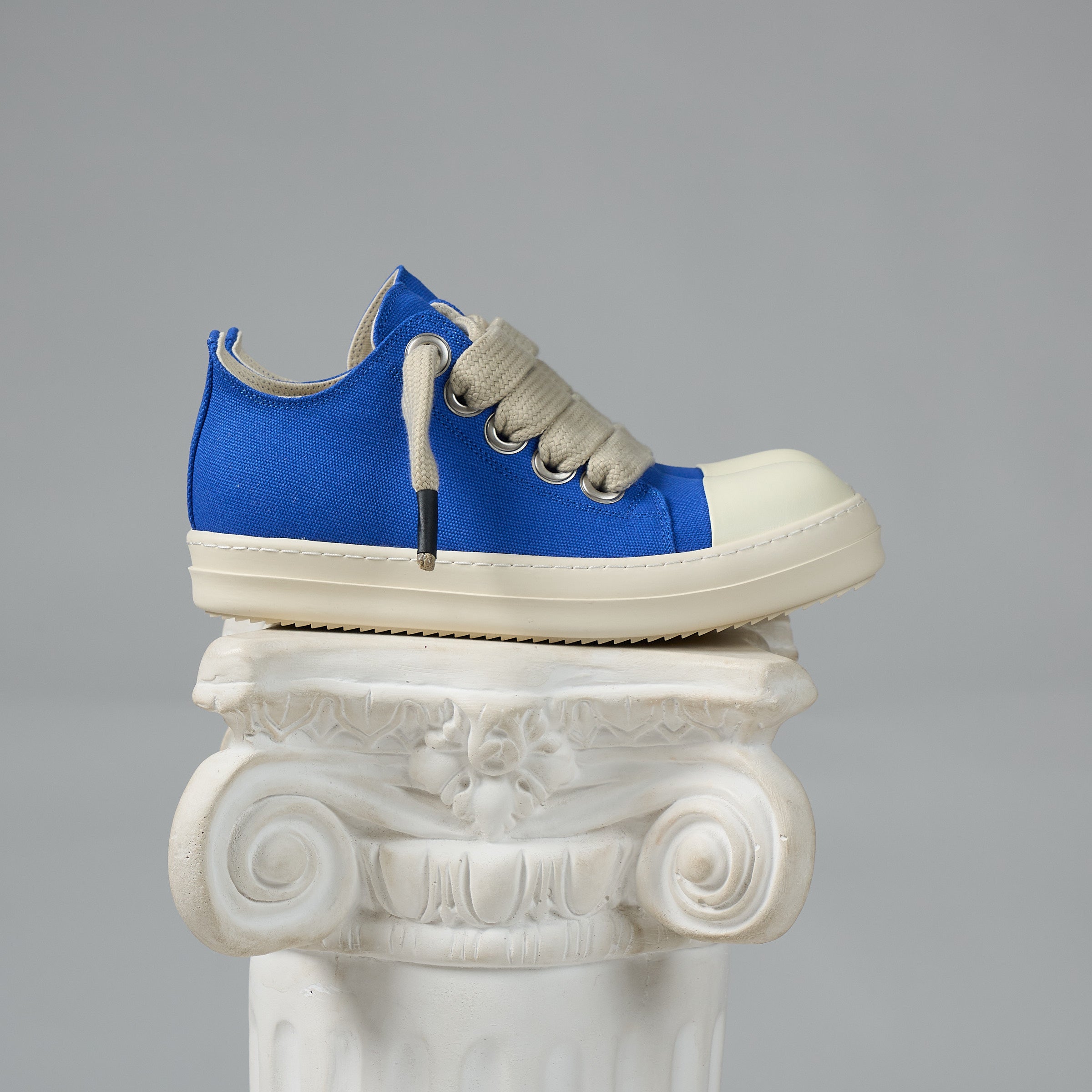 DUAA Blue and white sneaker on a decorative white column against a gray background