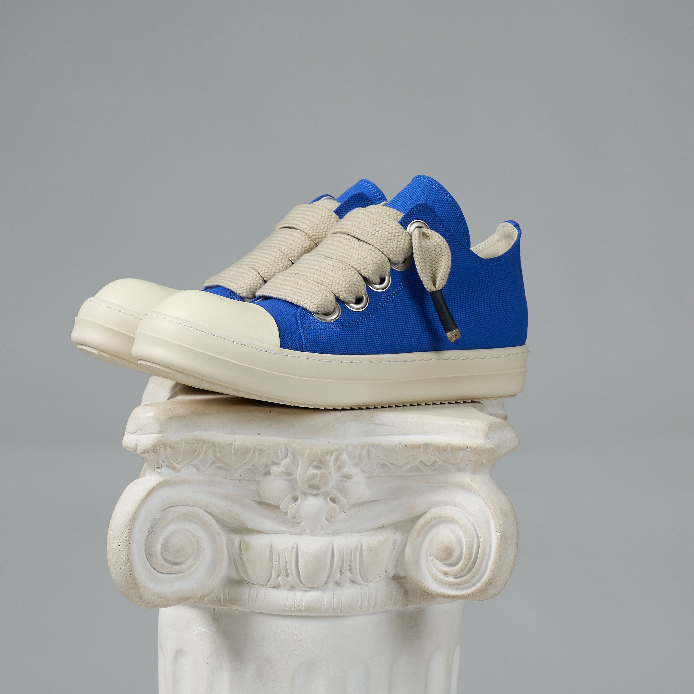 DUAA Blue and white sneakers on a decorative white column against a gray background