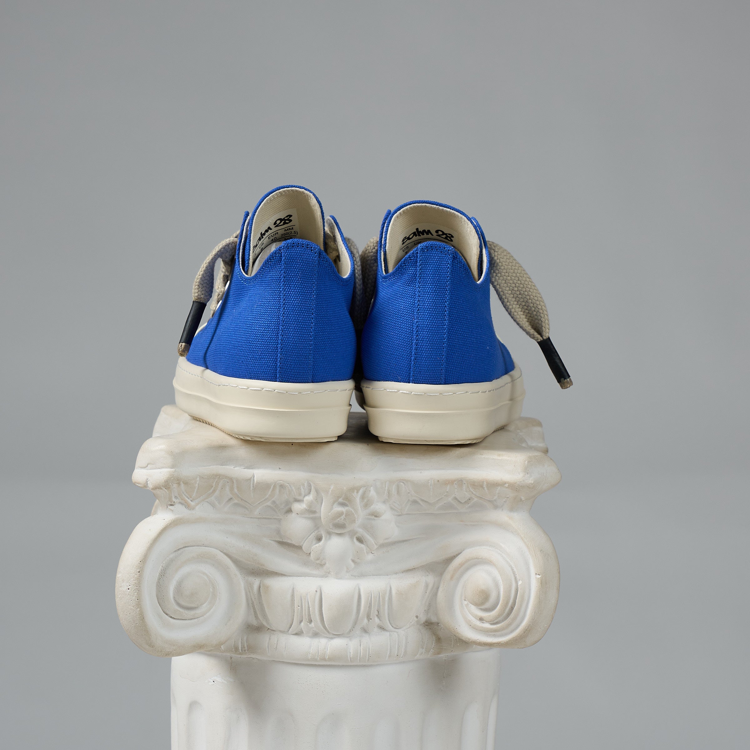 DUAA Blue sneakers with white soles on a decorative white column against a gray background