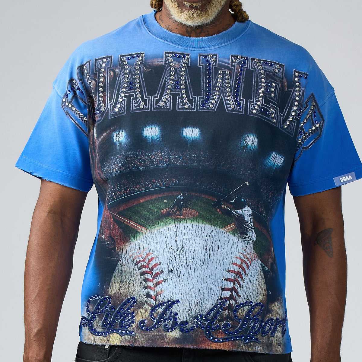 Man wearing a blue graphic t-shirt with sunglasses and braided hair on a plain background