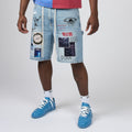 A person wearing light-wash denim shorts covered with graphic patches and stickers, paired with white socks and blue sneakers, photographed against a light gray studio background.